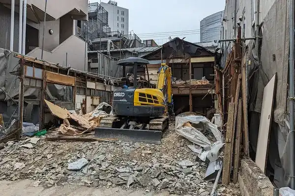 Pelleteuse démolissant une petite maison entre deux immeubles
